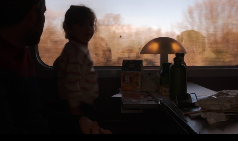 photographie avec flou artistique petite fille du train tgv sncf montpellier-perpignan par barbara ferreres, fujifilm, 2023. Une jeune fille et son siège en contre jour, la lumière de la première classe aussi, laissant échapper une transparance jaune. Les noirs sont dont des tons plutôt sépias et violets, rappelant le ciel et les arbres sans feuilles qui composent le paysage d'hiver qu'elle regarde par la fenêtre du train par barbara ferreres fujifilm xs10 photo of a small girl looking by the window of the train montpellier-perpignan, seeing a southern winter scenery with a blue sky and trees with brown leaves if any, soft picture taken against the light in sepia tones with the violet hue of the train, matching the brown leaves of the treas. photography taken by barbara ferreres with a fujifilm camera